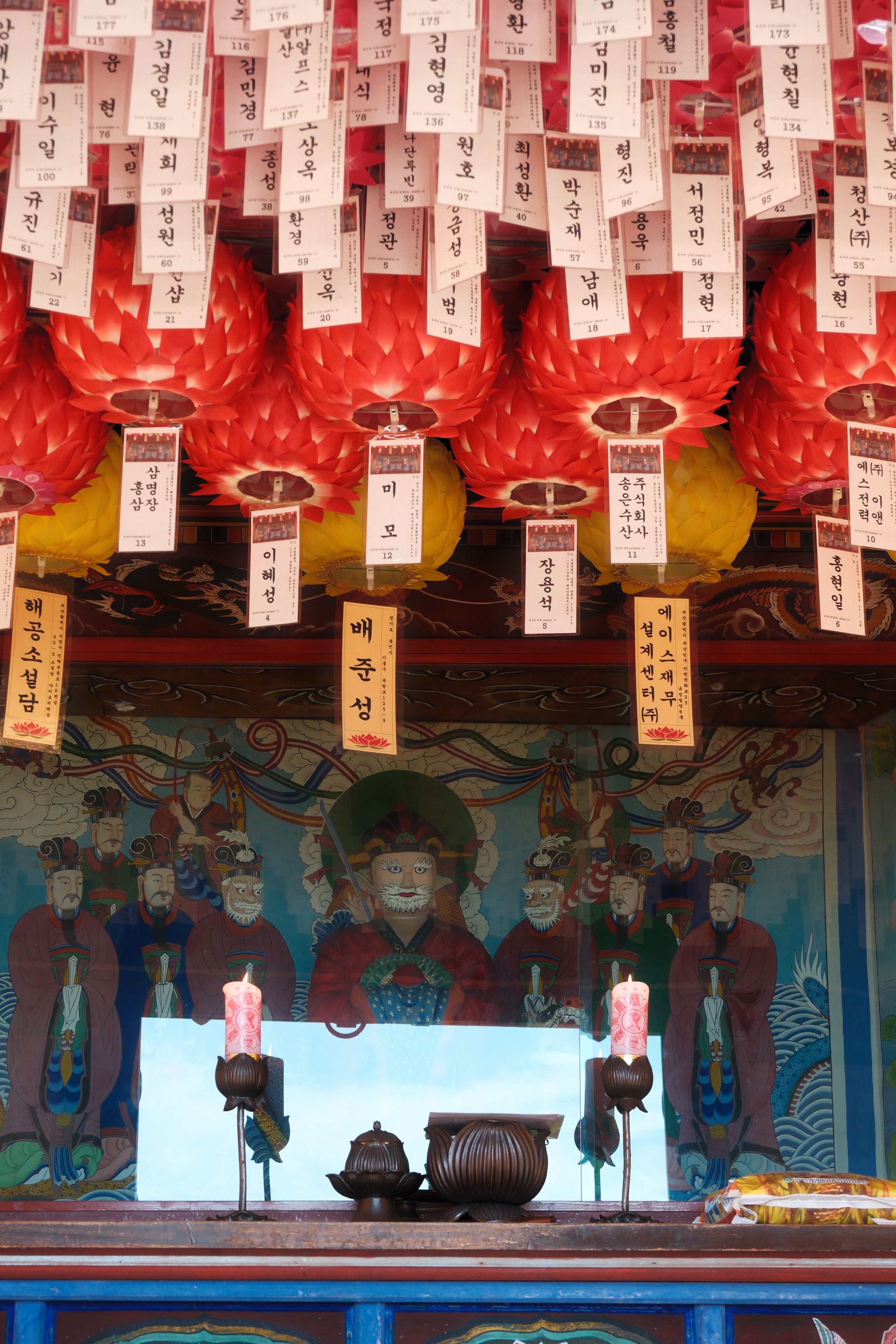 Vibrant interior of a Korean temple with red lanterns, traditional artwork, and paper notes.