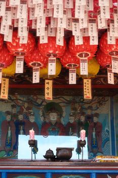 Vibrant interior of a Korean temple with red lanterns, traditional artwork, and paper notes.
