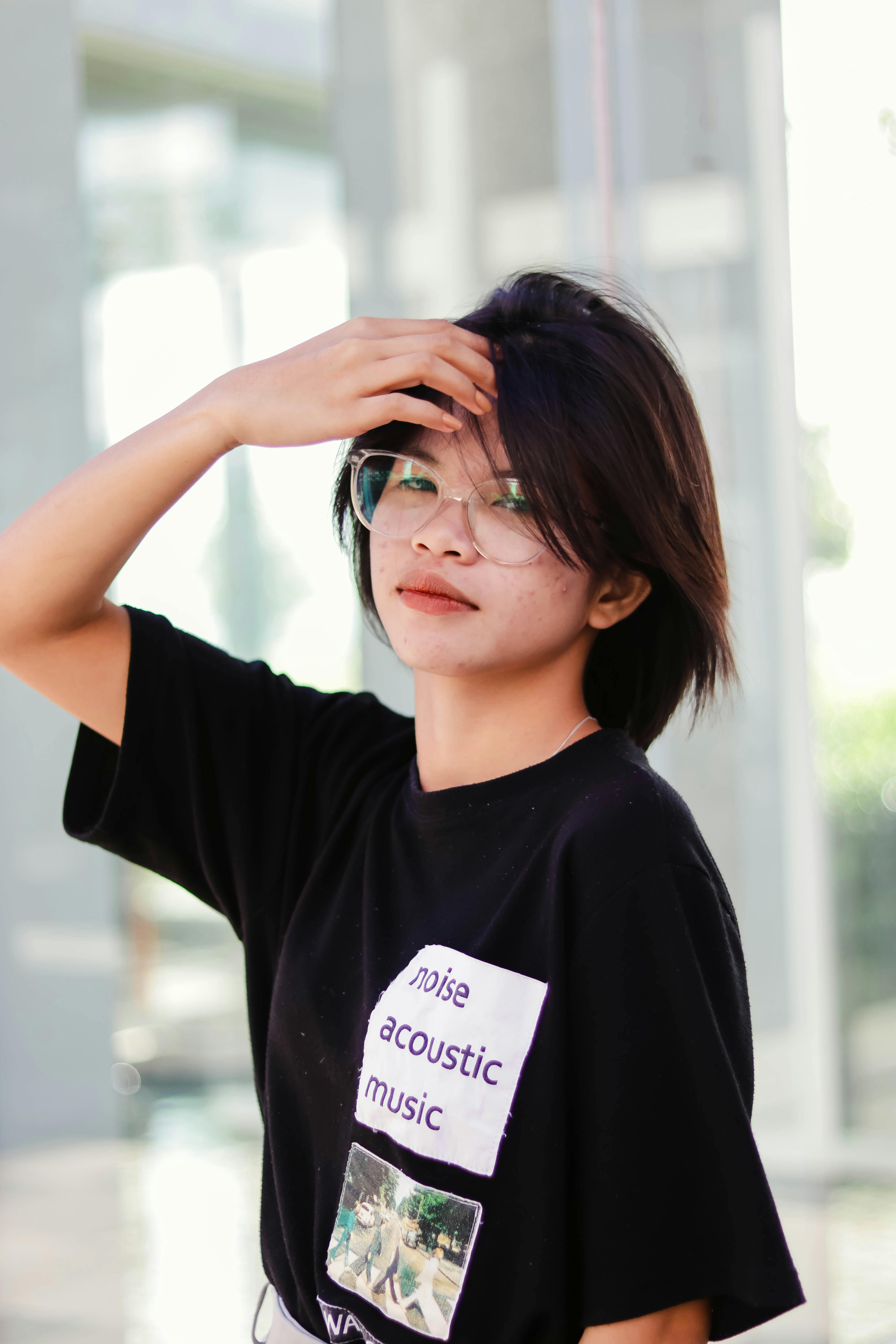 Young woman with glasses poses confidently in a black shirt with music-themed print.