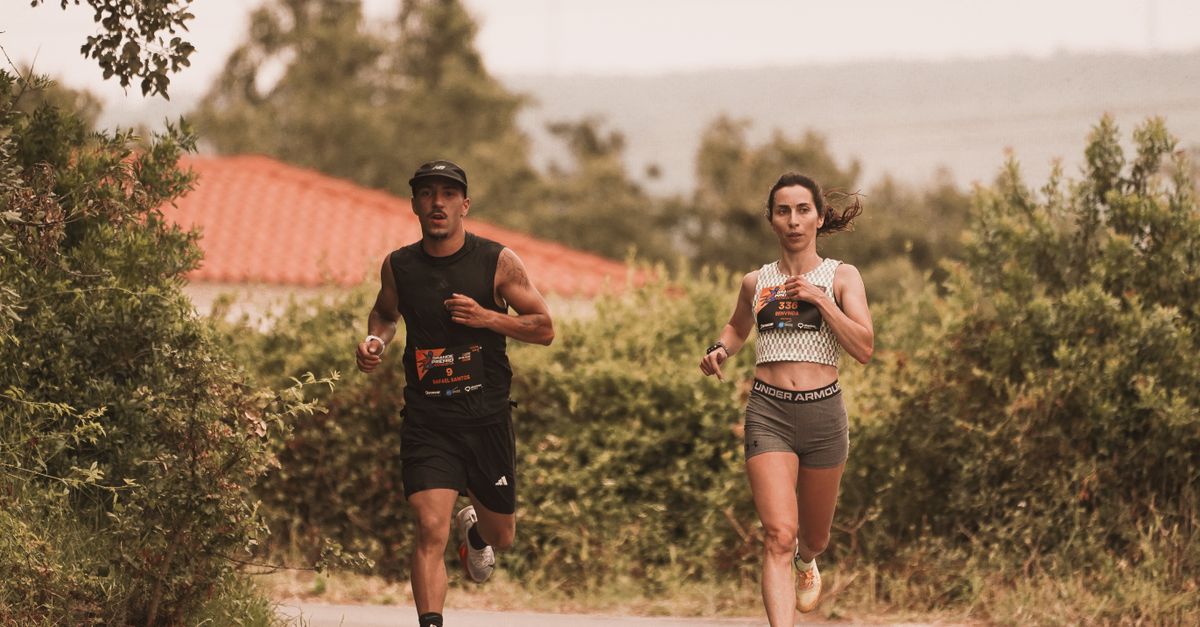 Two athletes jogging on an outdoor trail during a marathon, surrounded by greenery.
