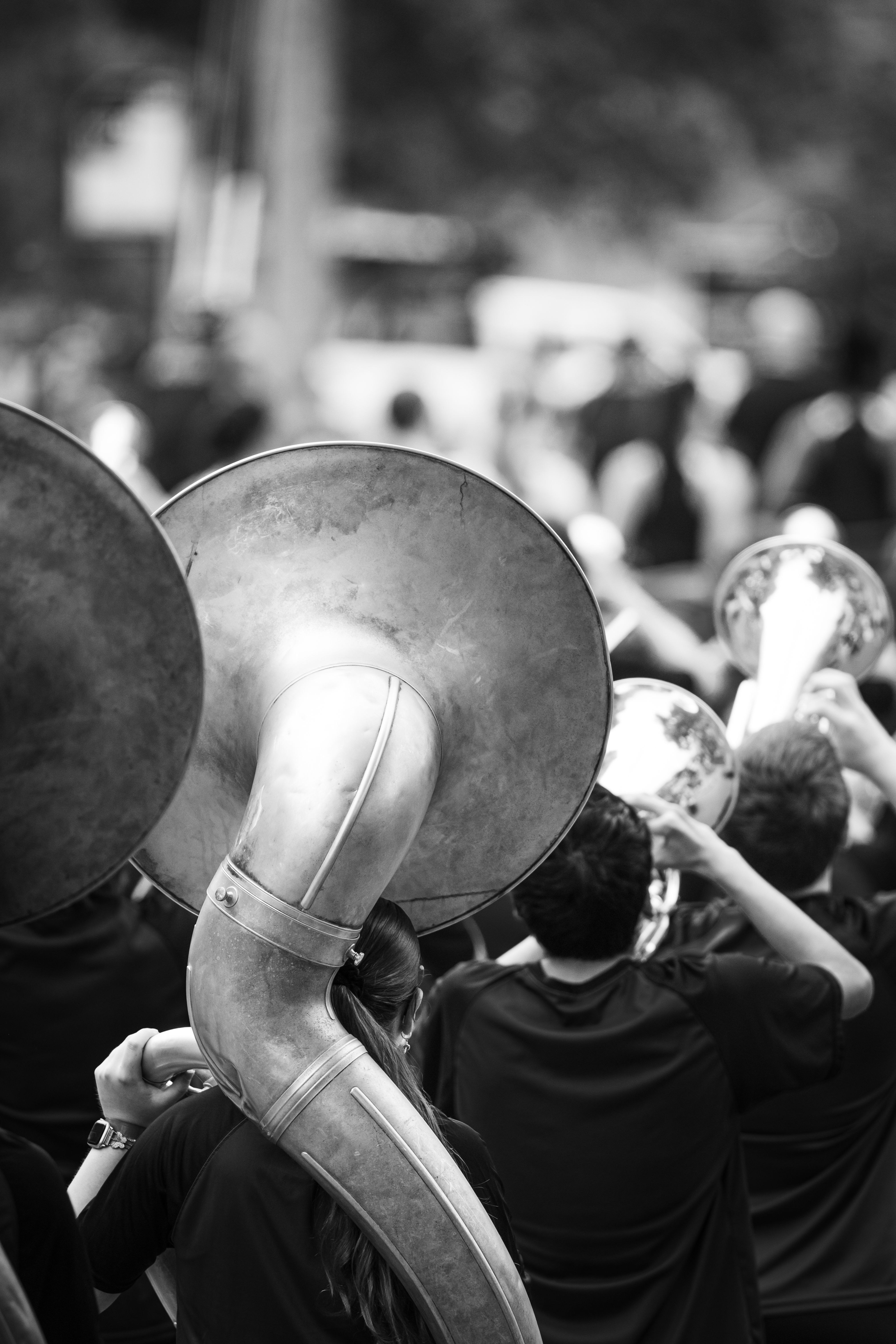 Black and white photo of a marching band with musicians playing brass instruments during a parade.