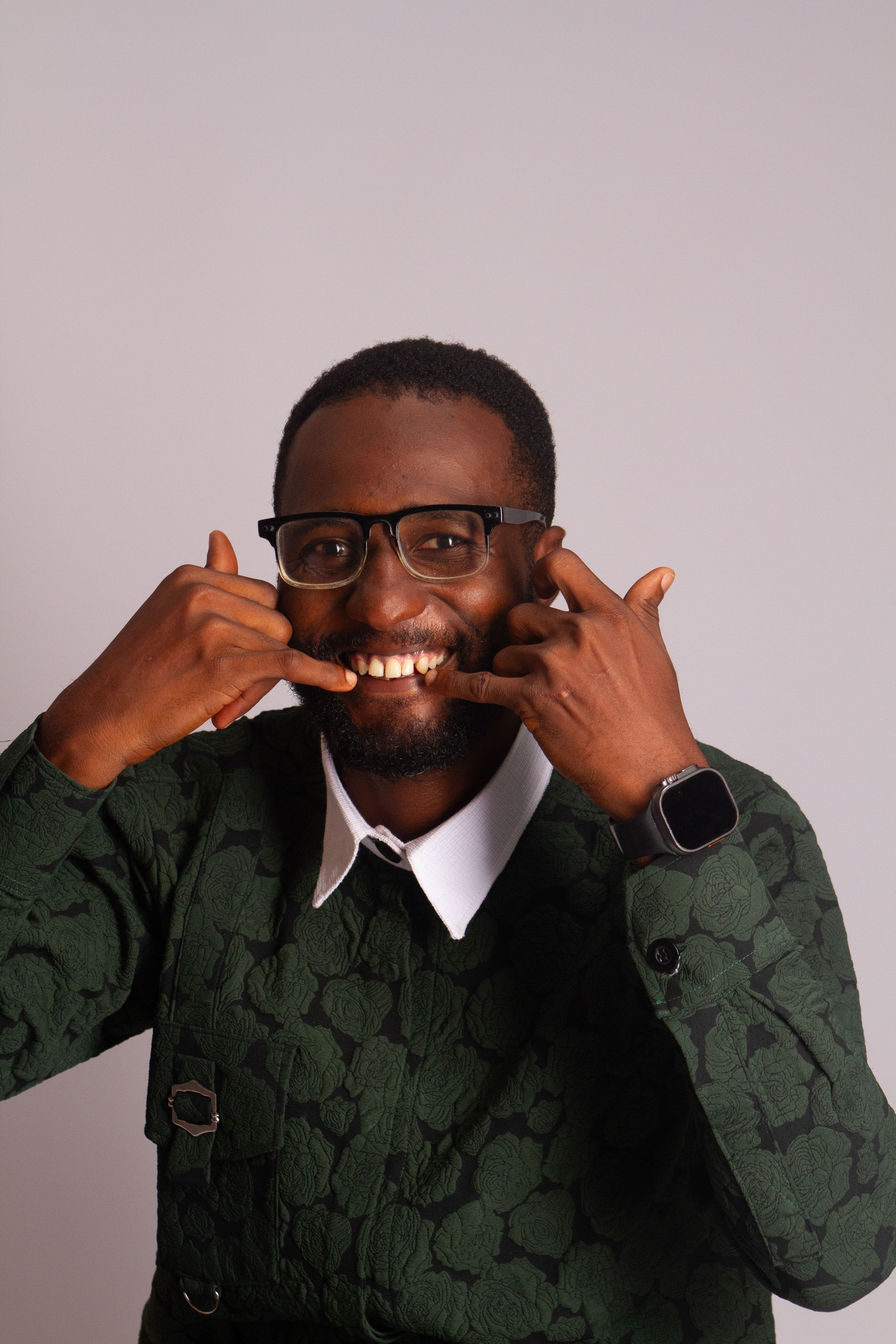 A cheerful adult man wearing glasses and a green outfit poses playfully against a neutral background.
