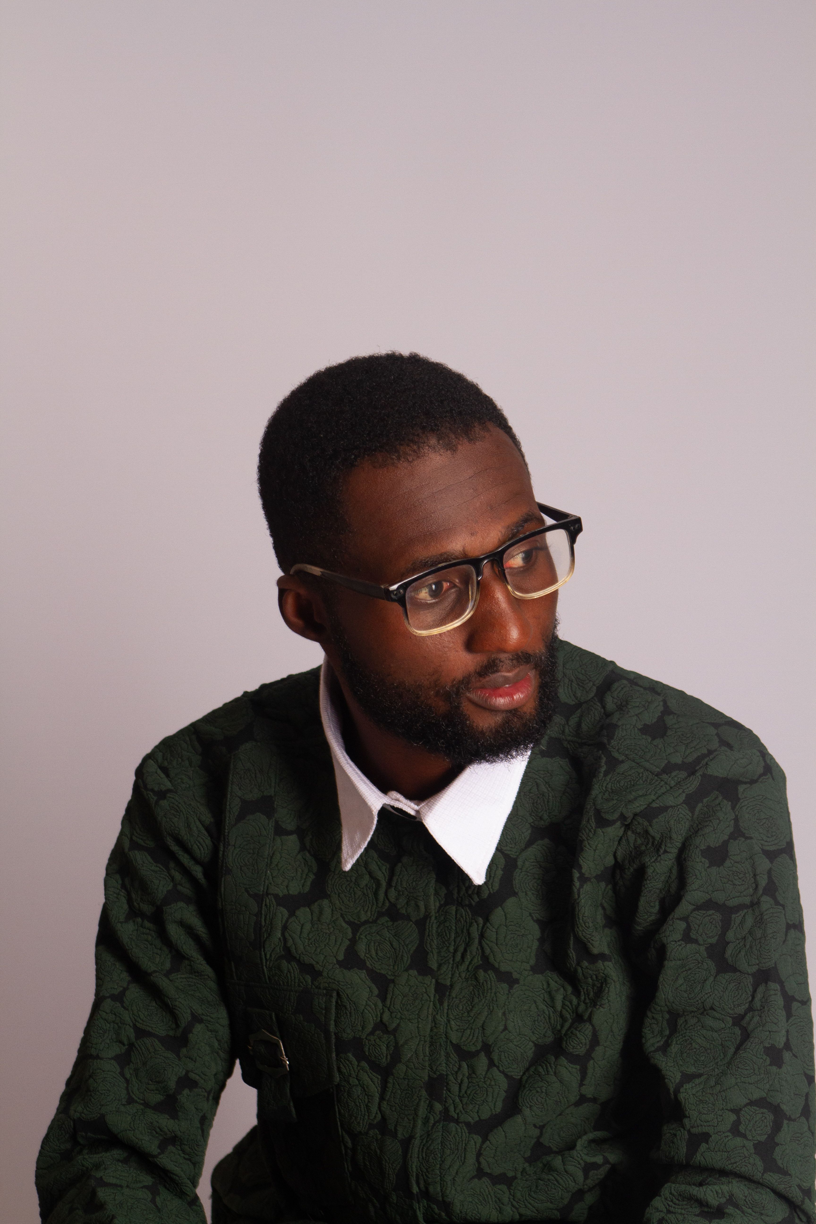 Stylish man wearing glasses and a green sweater with a thoughtful expression.