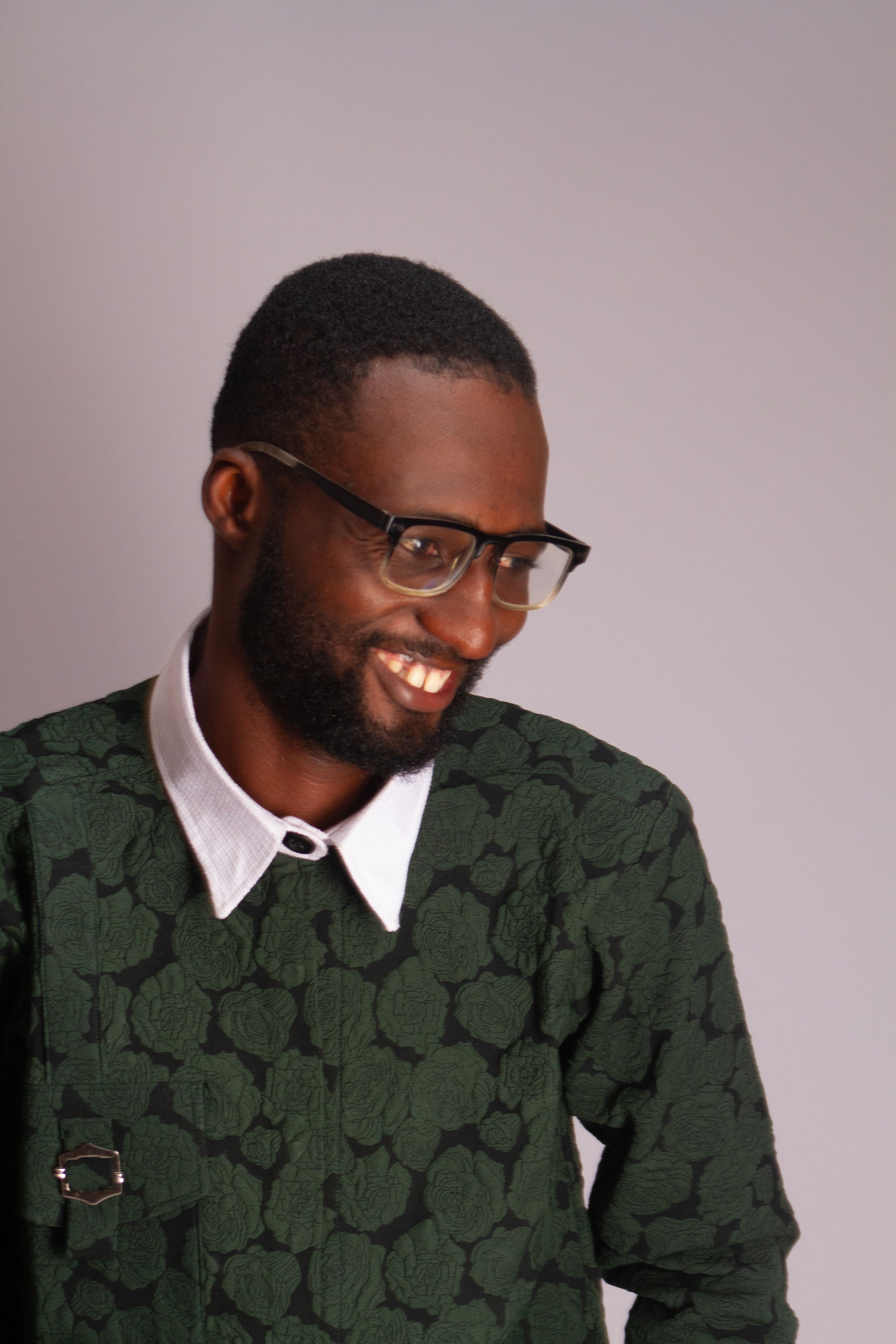 Portrait of a smiling young man in a green patterned shirt, exuding confidence and style.