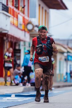 Determined runner covered in mud participating in an urban marathon race with colorful architecture.