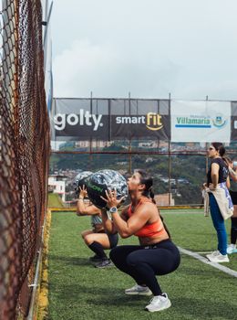 Women engage in outdoor fitness training with medicine balls on a grassy field under cloudy skies.