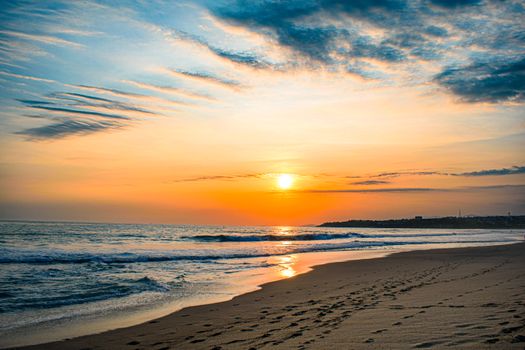 A tranquil beach scene at sunset with footprints in the sand and colorful sky.