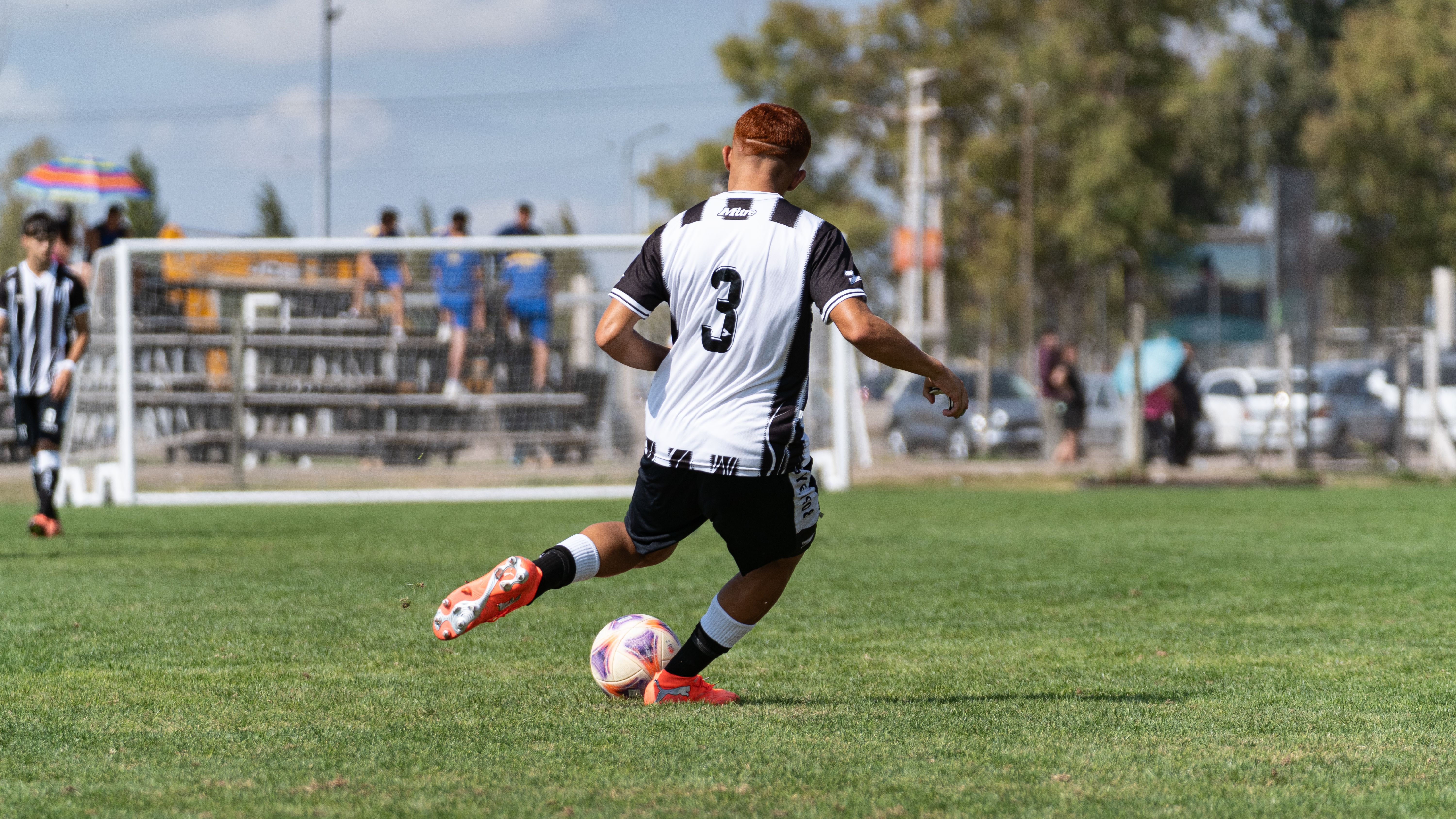 Action shot of a young soccer player wearing number three during a match on a sunny day.
