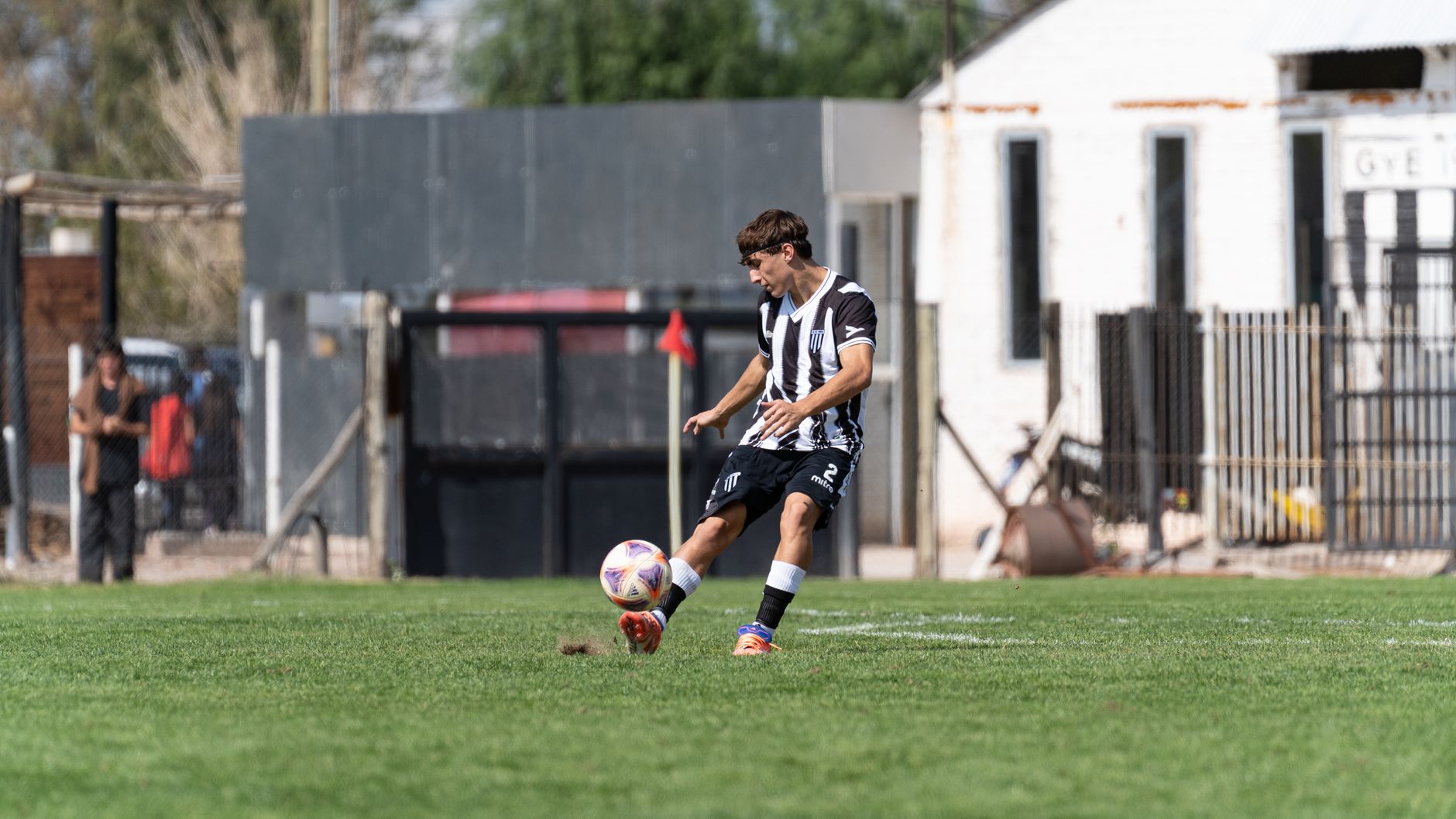 Dynamic action shot of a young male soccer player kicking a ball during a daytime match on an outdoor field.