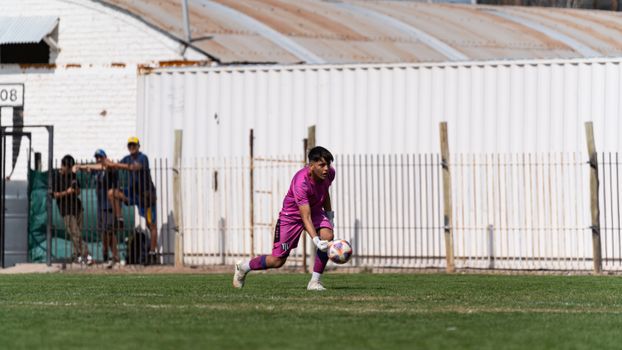 Young goalkeeper wearing pink kit prepares to make a save on a sunny day.