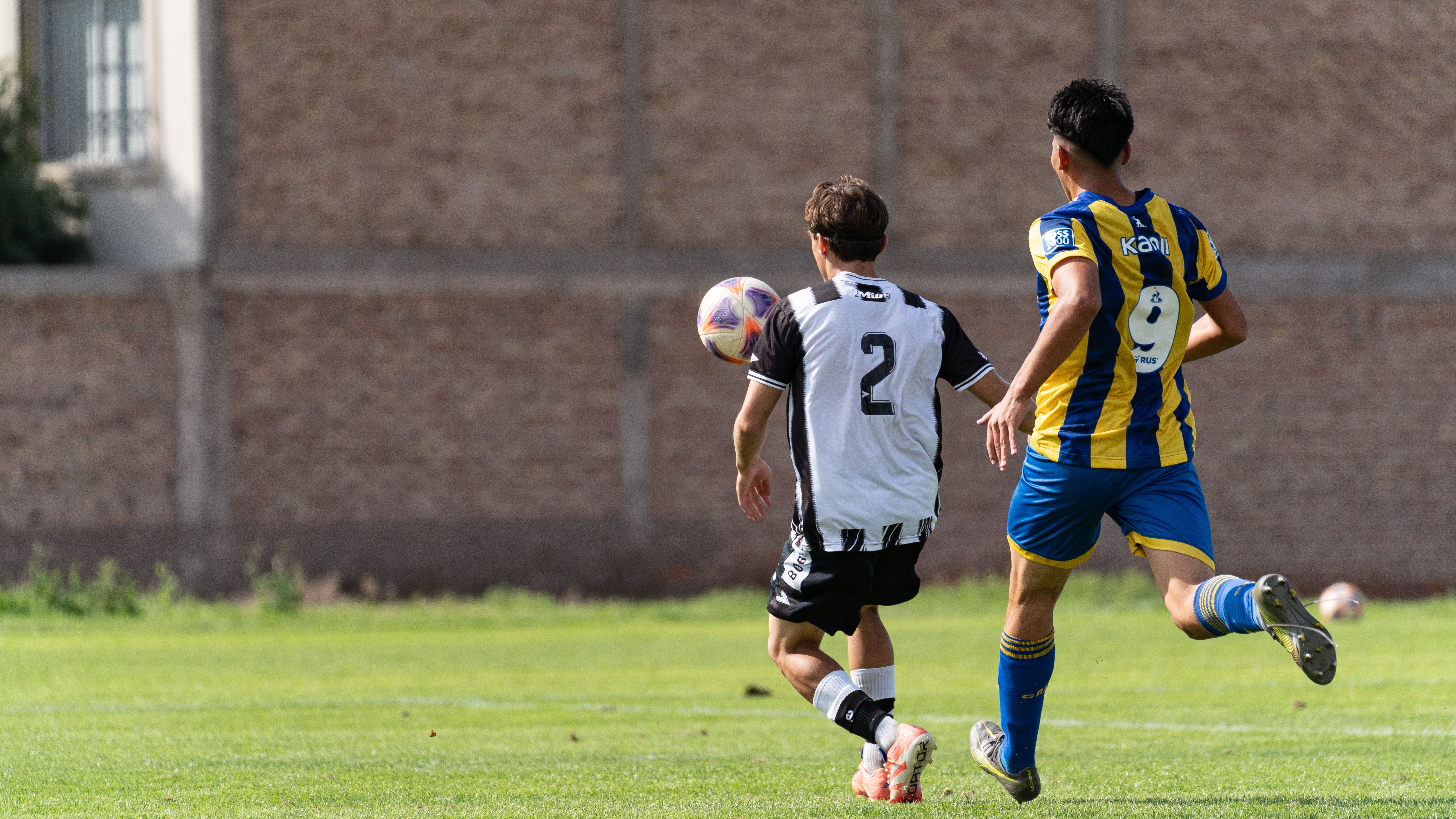 Two soccer players challenge for the ball during an outdoor game, showcasing athletic action.