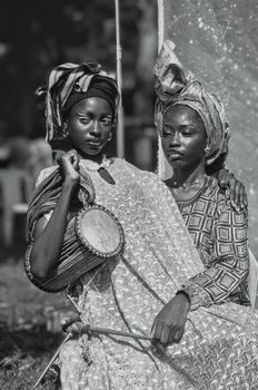 Two Nigerian women in traditional attire holding a drum, depicting cultural heritage in Nigeria.