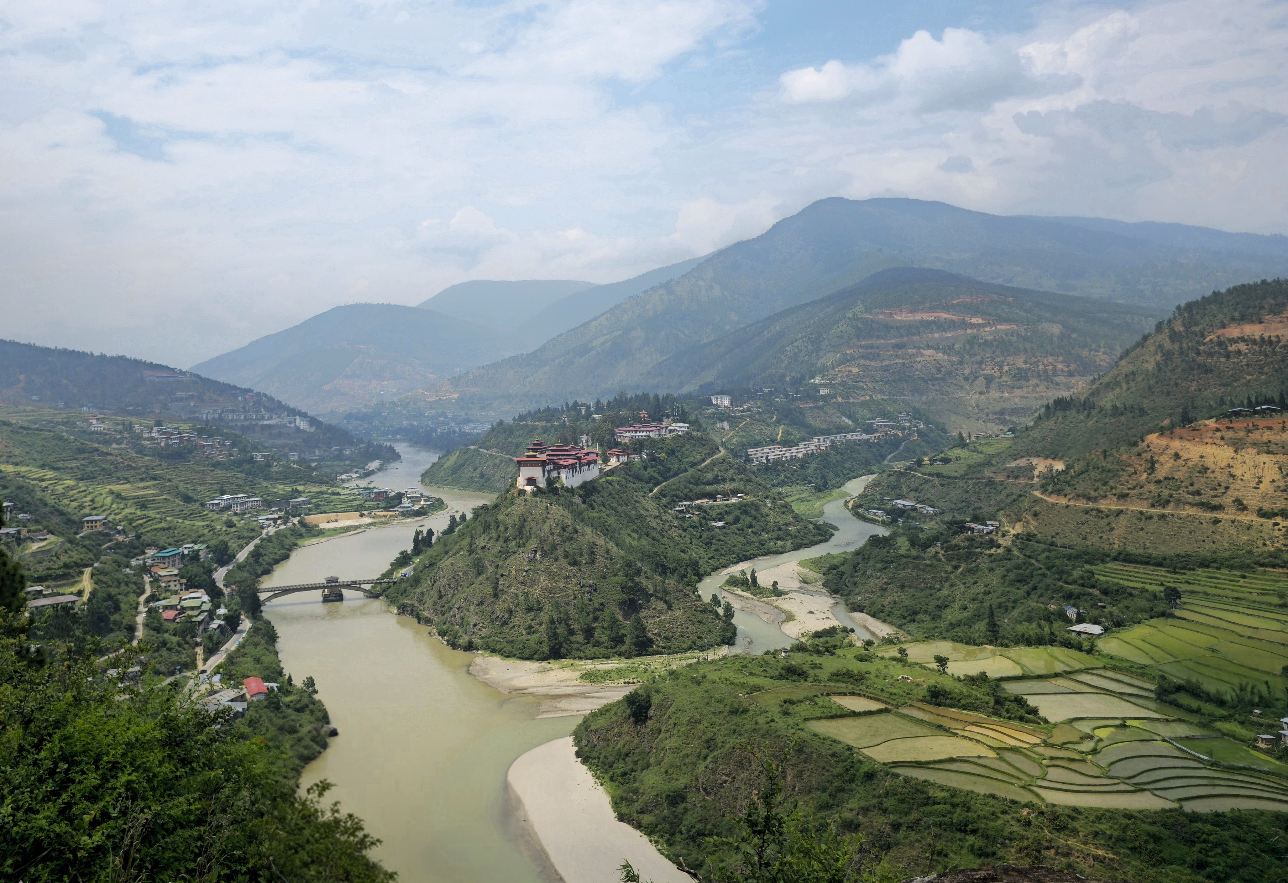 Scenic view of Punakha Valley with Mo Chhu River and rice paddies, lush greenery and distant mountains.