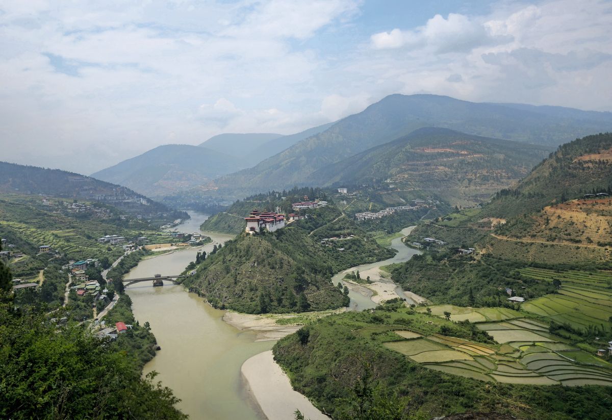 Scenic view of Punakha Valley with Mo Chhu River and rice paddies, lush greenery and distant mountains.