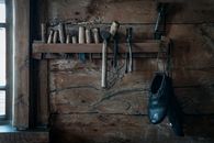 Shoemaker tools hanging on shelf in rustic wooden workshop