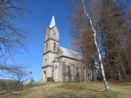 Free Stone church in Szklarska Poręba surrounded by trees under bright blue sky. Stock Photo