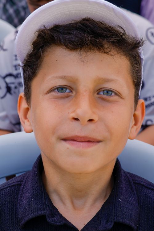 Free Close-up portrait of a young boy with striking blue eyes wearing a cap, smiling softly. Stock Photo