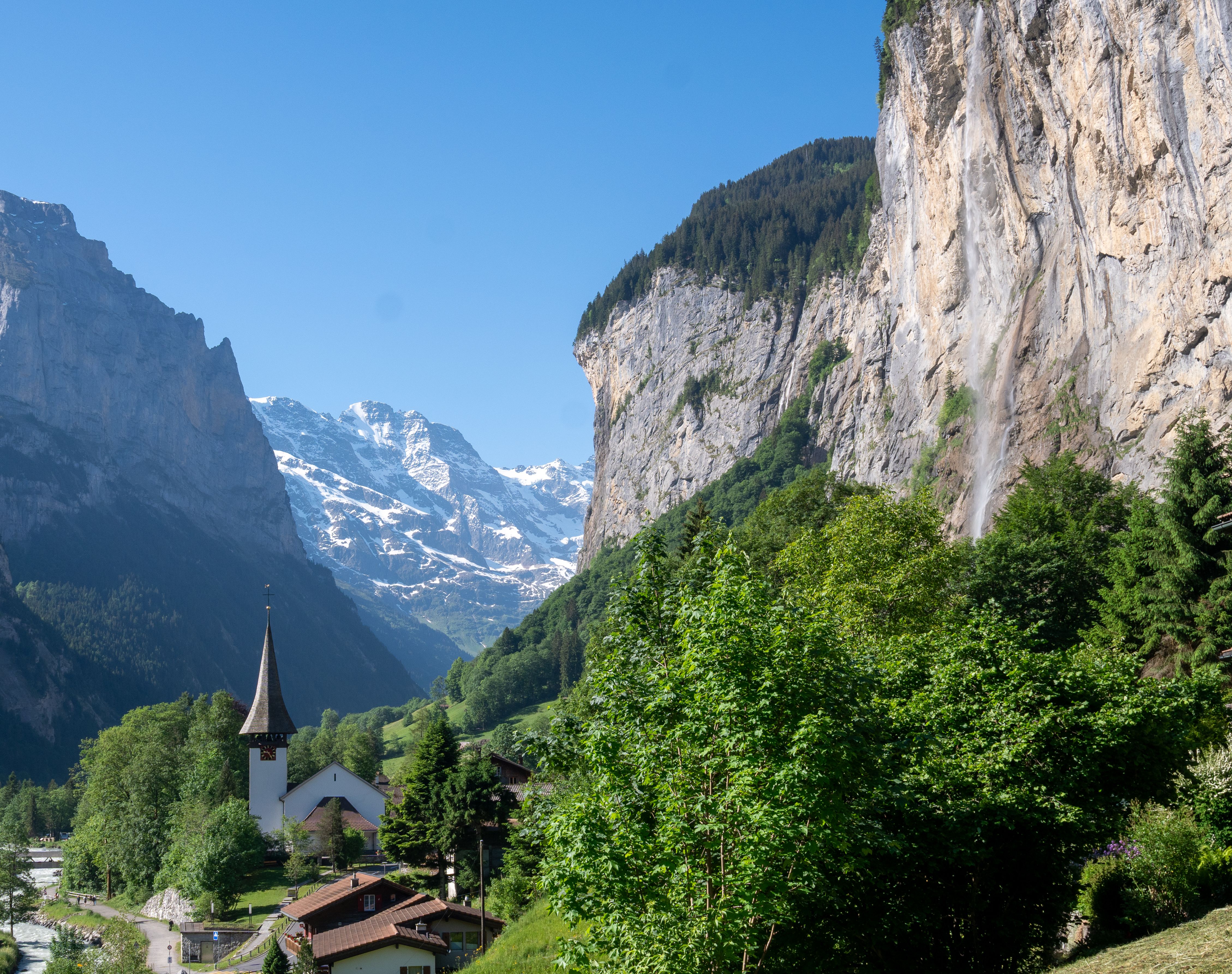 Alpine landscape of Lauterbrunnen Valley with church, mountains, and waterfall on a clear summer day.