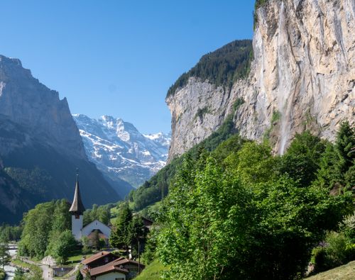 Alpine landscape of Lauterbrunnen Valley with church, mountains, and waterfall on a clear summer day.