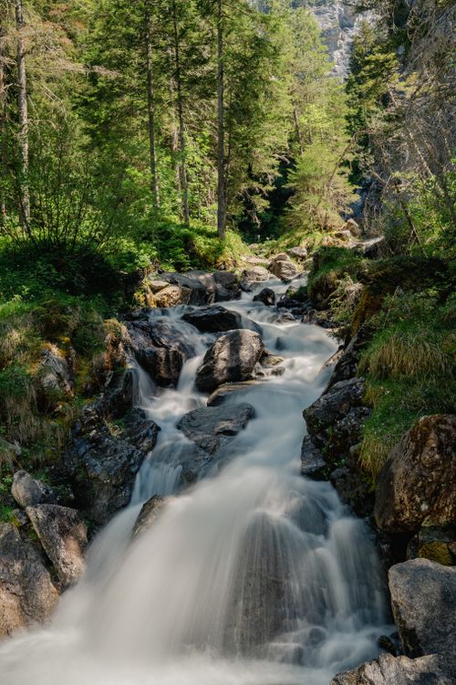 Free Peaceful forest scene with a cascading waterfall flowing over rocks surrounded by lush greenery. Stock Photo