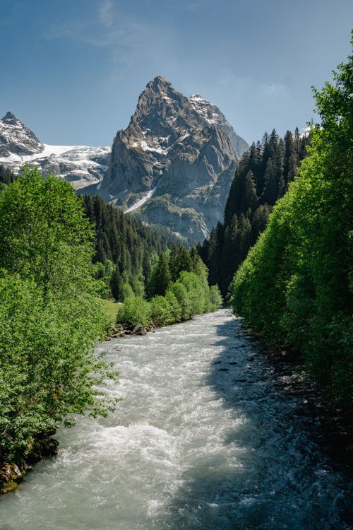 Free Serene alpine river flowing with snow-covered mountains in the background. Stock Photo