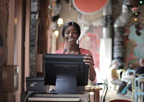 A woman is standing behind a counter in a restaurant holding a computer monitor.