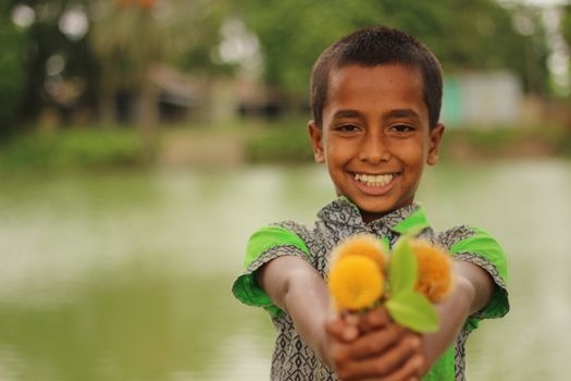 Joyful child holding yellow flowers beside a serene pond, smiling warmly.