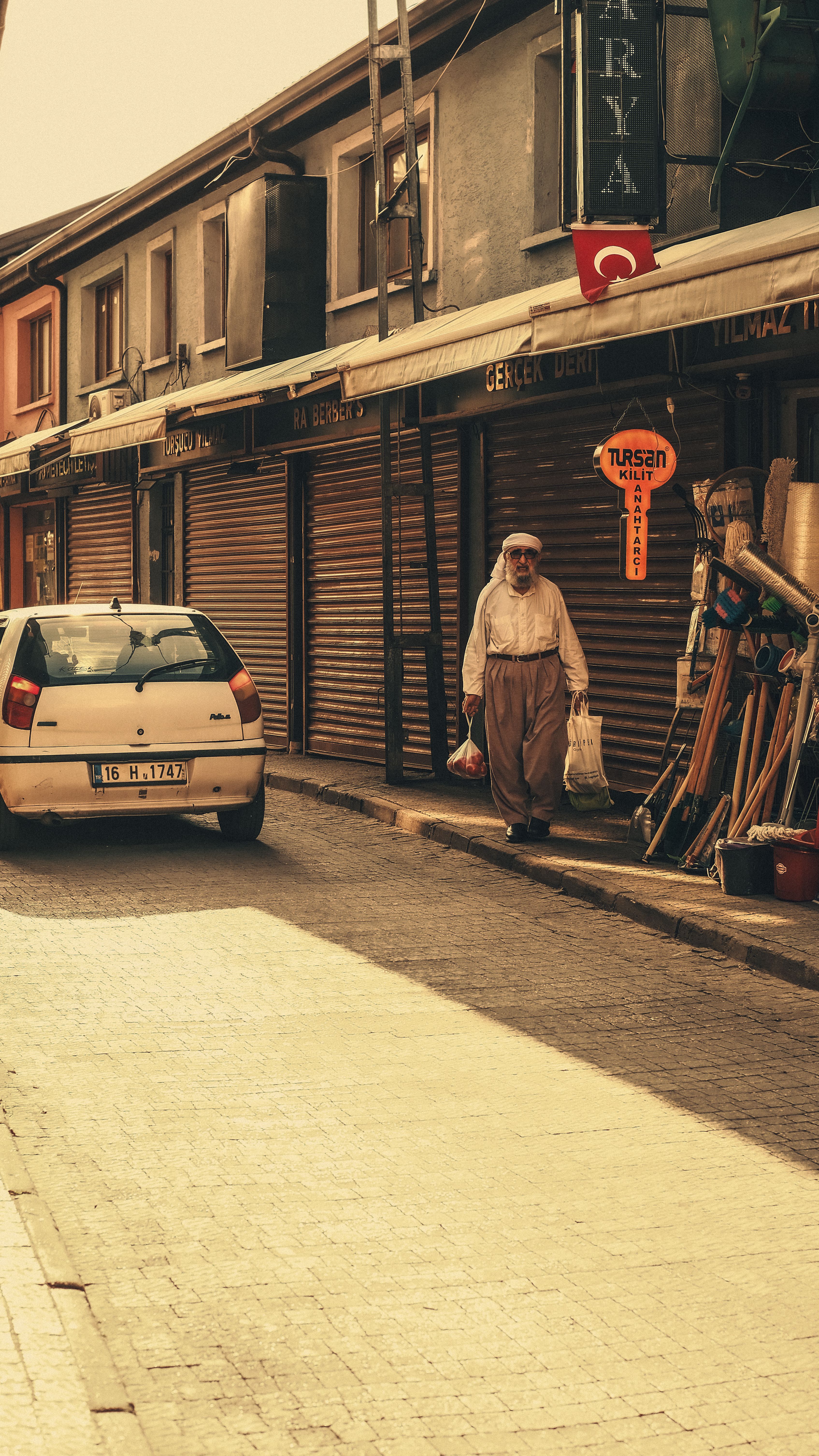A serene street scene capturing an elderly man walking in a Turkish neighborhood, lined with closed shops.