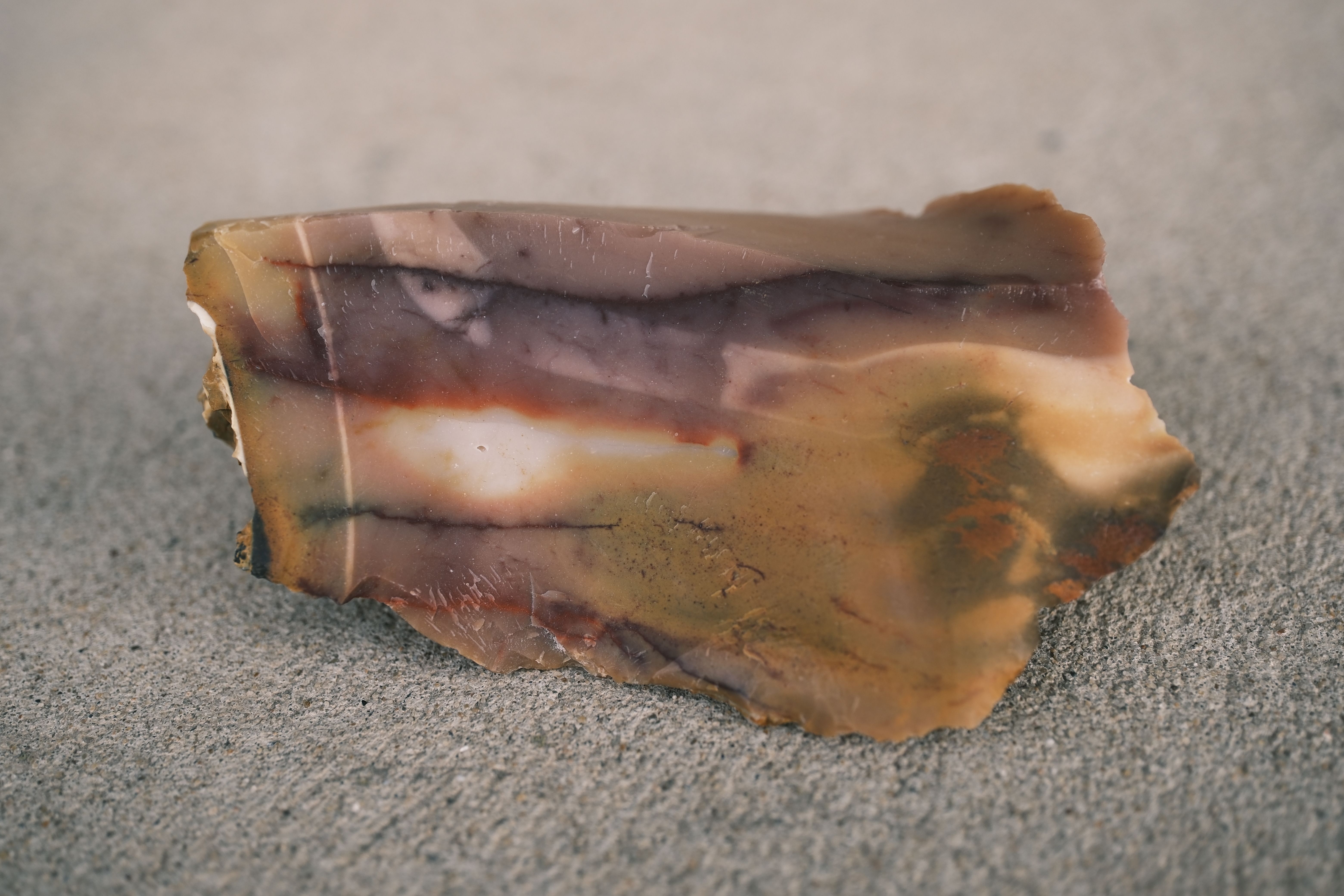 Close-up of a natural rough stone showcasing earthy tones and textures on a concrete surface.