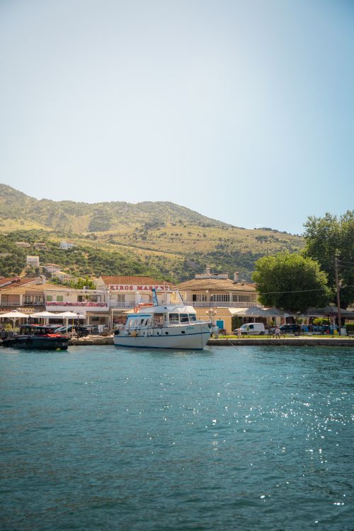Free Idyllic waterfront view featuring boats, clear waters, and a sunny Greek coastal village. Stock Photo