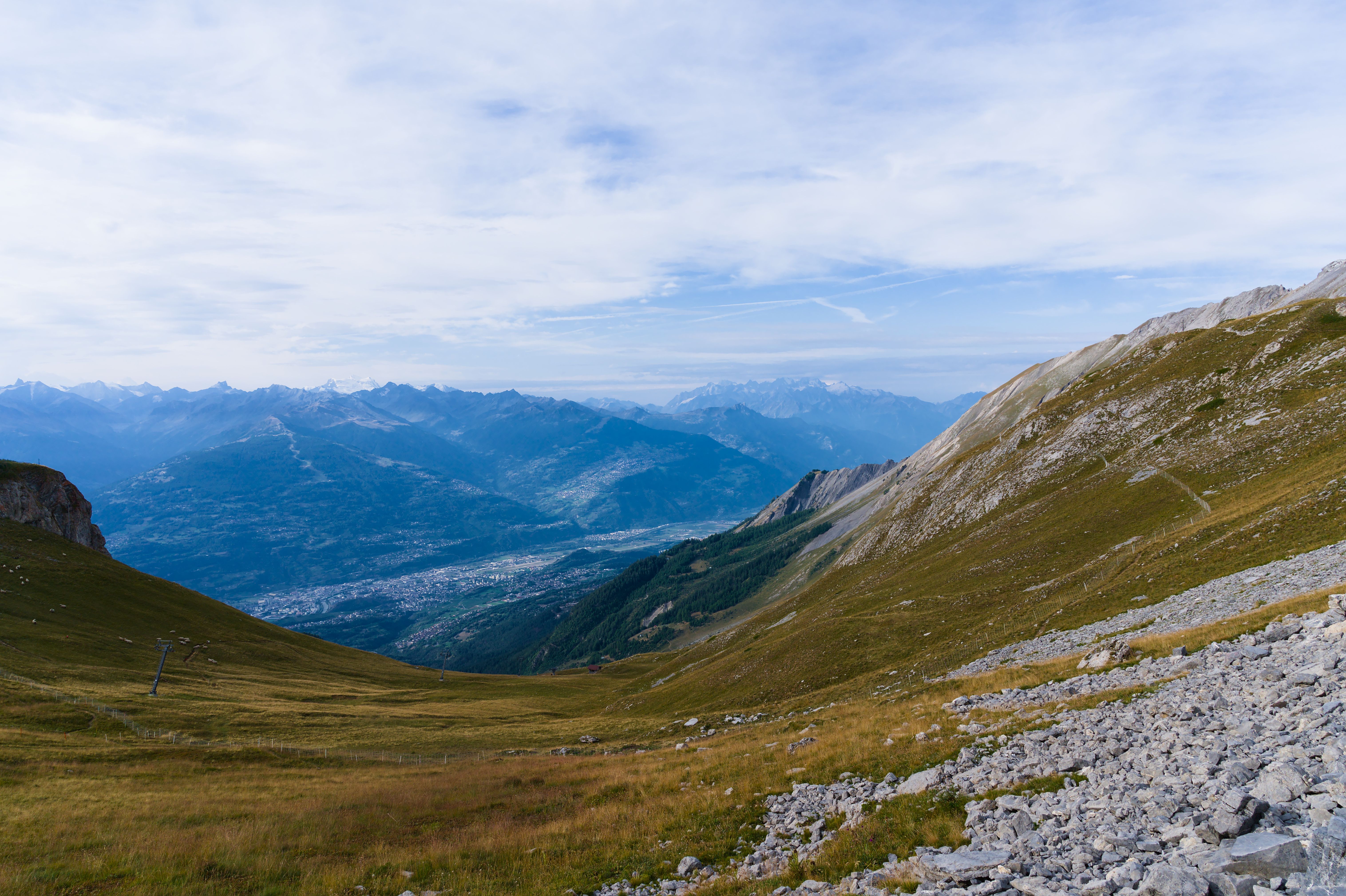 Beautiful alpine landscape with lush green valleys and distant mountain peaks under a cloudy sky.