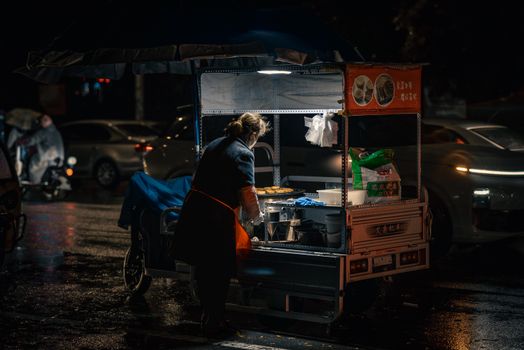 A vendor prepares food in a street cart at night, highlighting urban street food culture.