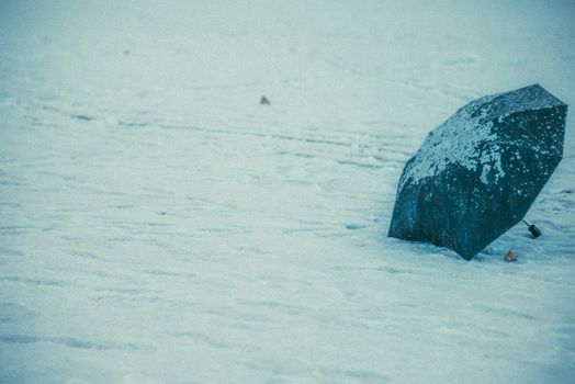 Green umbrella partially covered in snow on a wintry landscape.