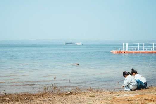 Two children enjoying a calm day by the lakeside, exploring nature.