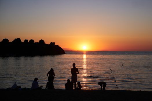 A serene sunset on a Greek beach with silhouetted figures enjoying the tranquil evening ambiance.