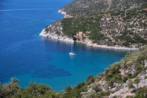 Free Peaceful bay in Greece with a boat anchored, surrounded by lush greenery and rocky coastline. Stock Photo