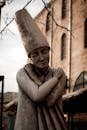 Stone monument of sorrowful female in tall hat hugging self located on street outside aged building on autumn day