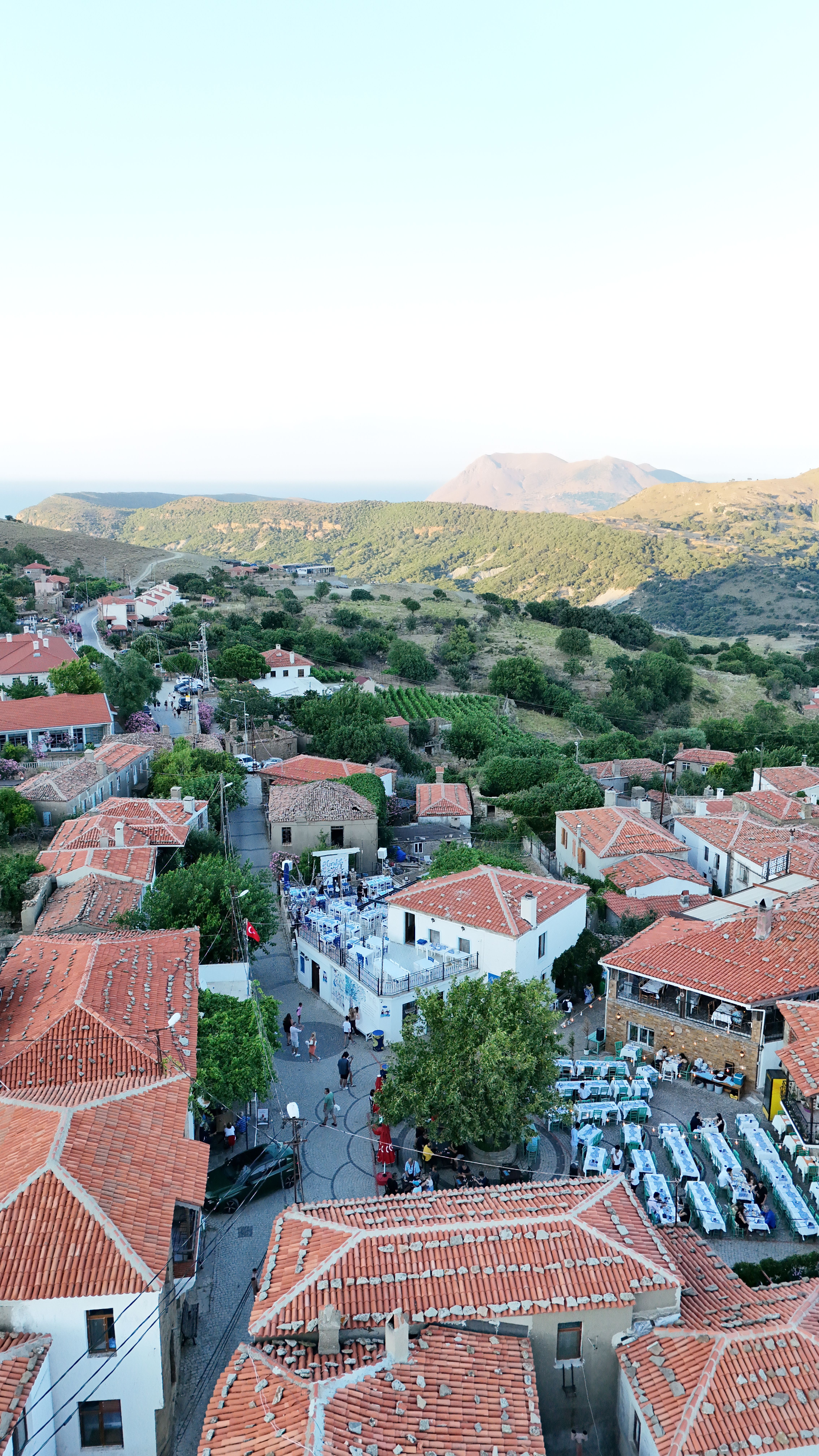 Scenic aerial view of a traditional village with red-tiled roofs in Gökçeada, Türkiye, surrounded by hills.