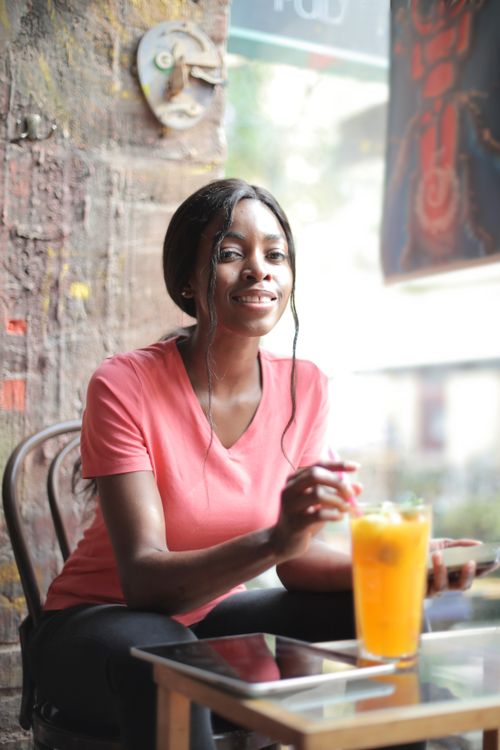 Free A cheerful woman in a pink shirt enjoys a glass of juice indoors, showcasing relaxation and happiness. Stock Photo
