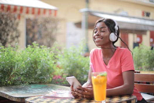 Joyful woman listening to music outdoors with headphones and fruit drink.