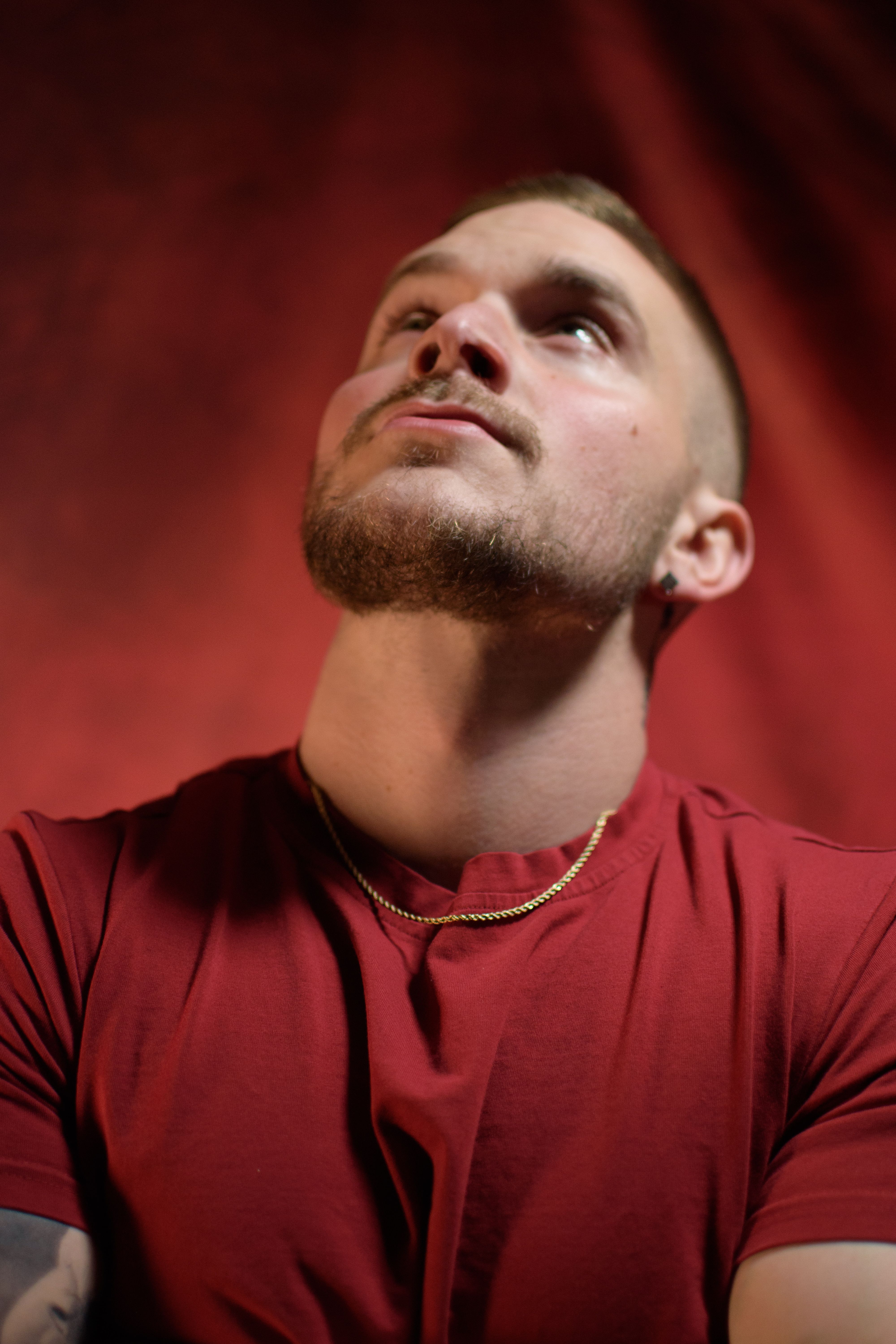 A thoughtful young man in a red shirt gazes upwards against a red background.