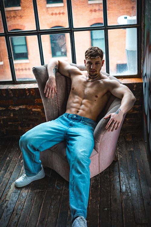 Free A man showcasing a fit physique relaxing in an industrial-style indoor setting with exposed bricks. Stock Photo