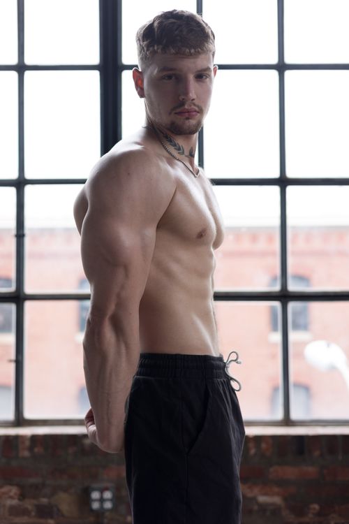 Free Portrait of a fit young man standing by a large industrial window, showcasing strength and fitness. Stock Photo