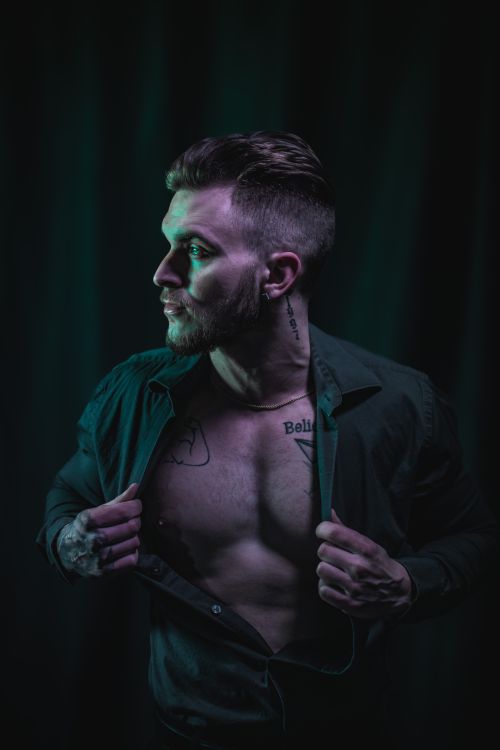 Free Chest-baring tattooed man in a dramatic low-light portrait, exuding mystery. Stock Photo