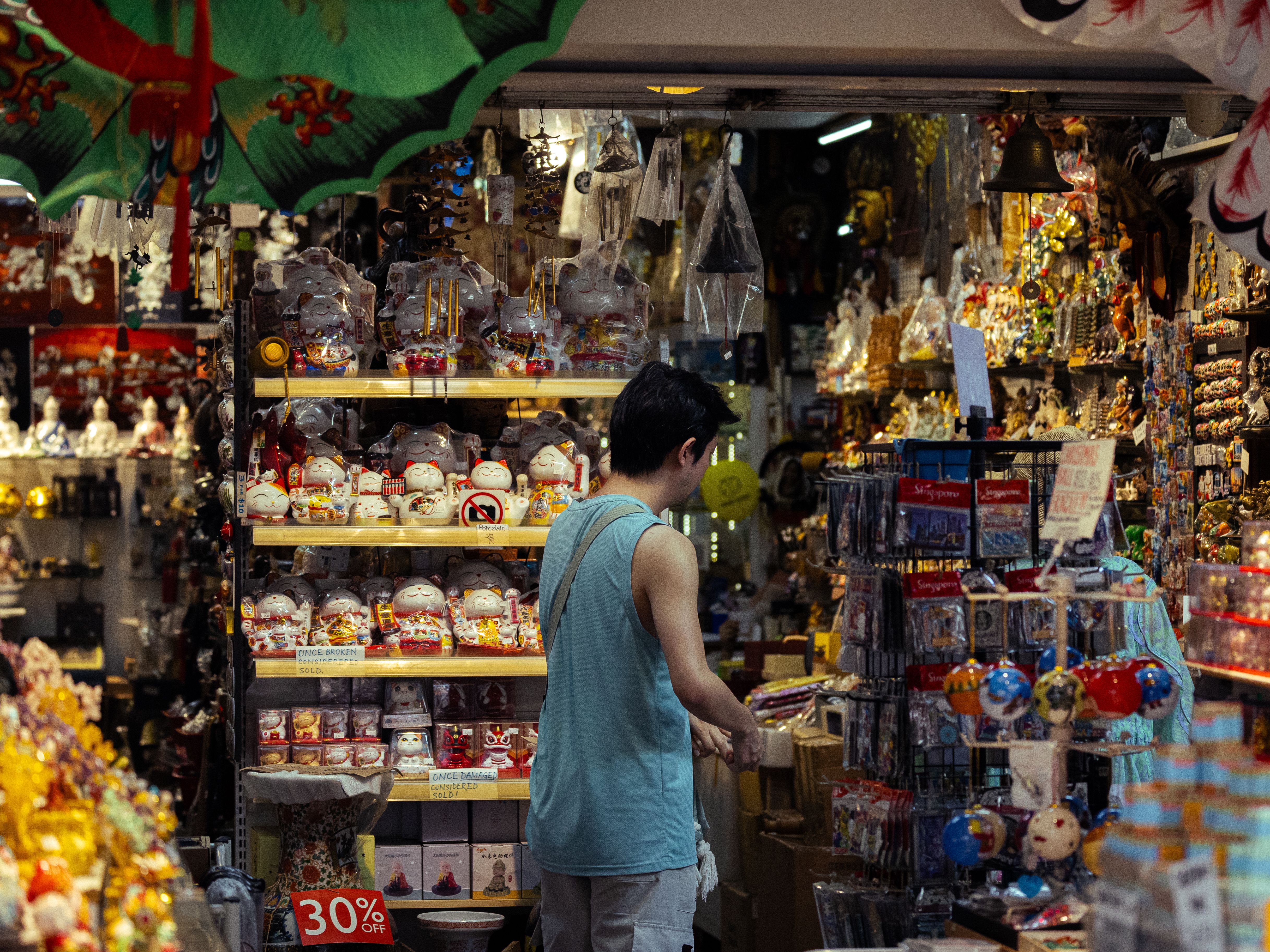 A man browses Asian souvenirs in a vibrant market store, surrounded by colorful items and decor.