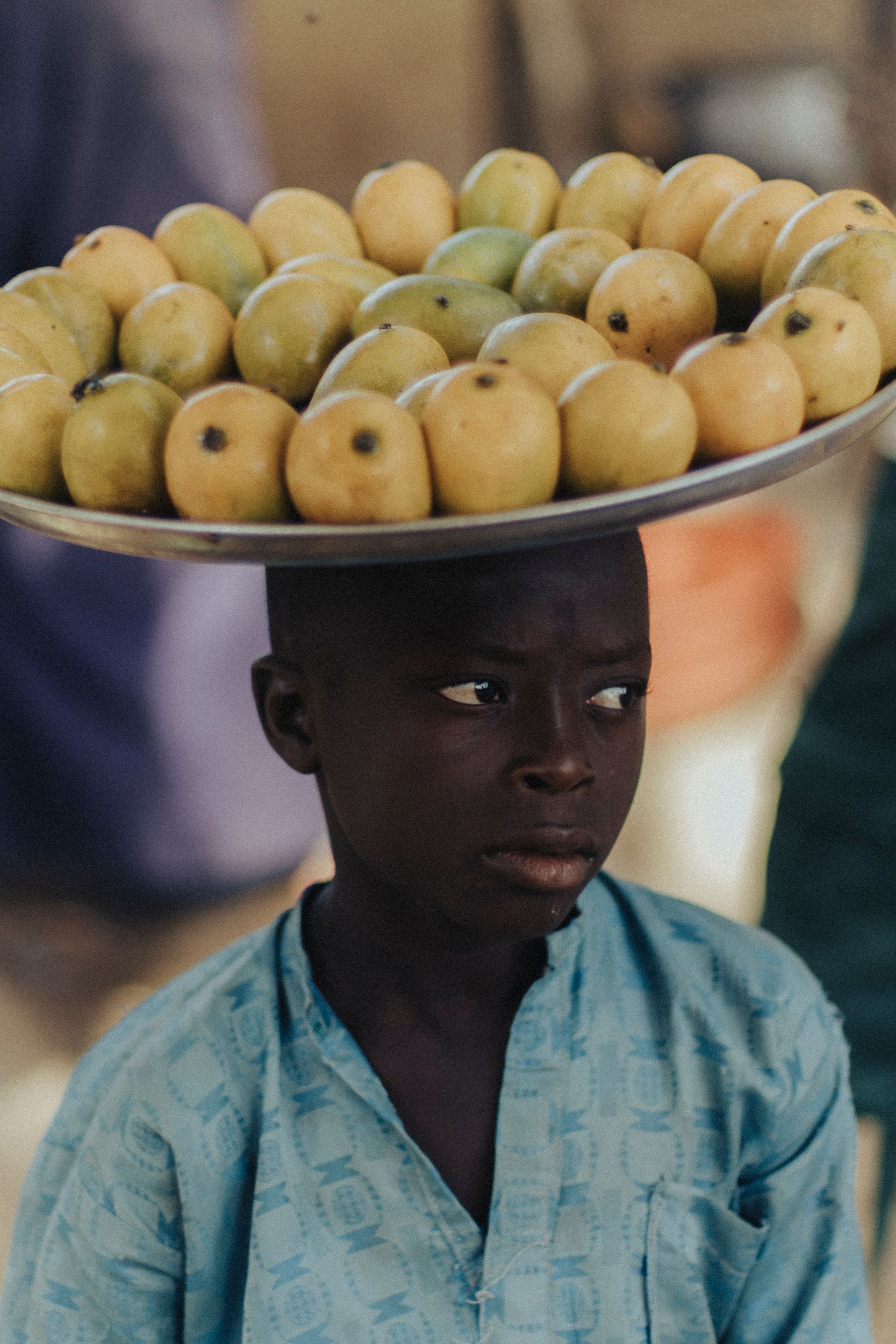 Un enfant marche avec un panier de fruits porté sur la tête