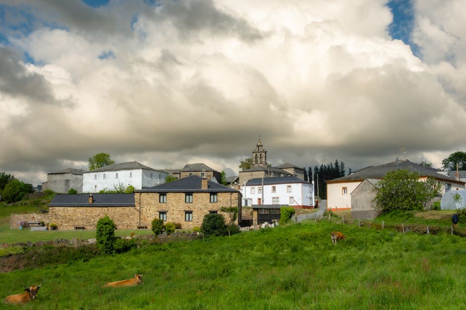Pintoresco pueblo rural con casas de piedra y exuberante vegetación bajo un espectacular cielo nublado.