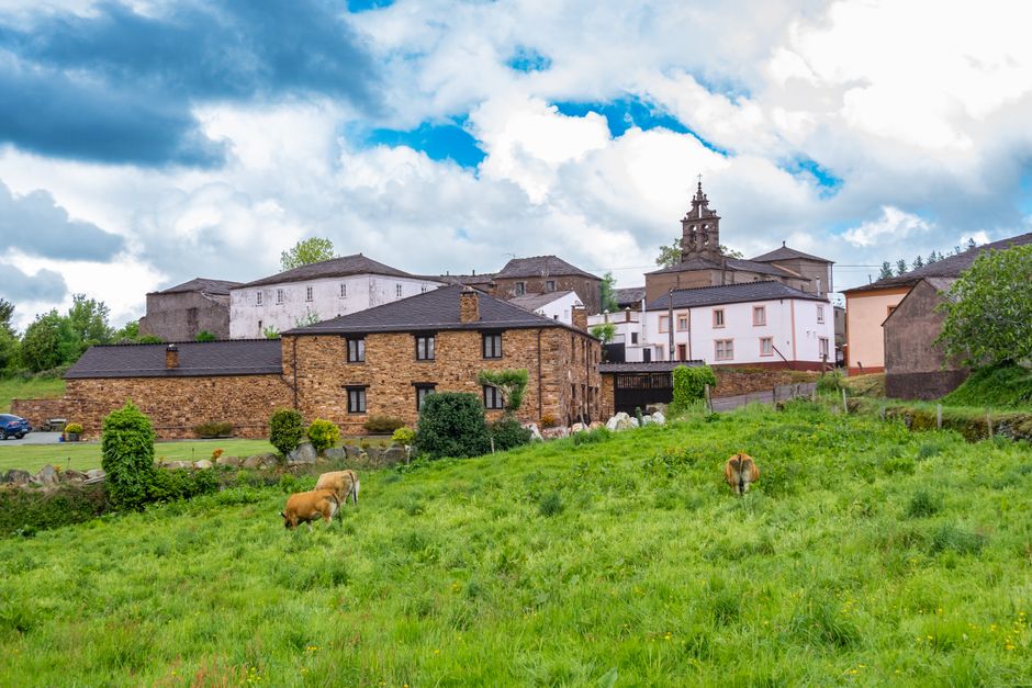 Pintoresco pueblo rural con casas tradicionales de piedra y vacas pastando en un campo verde y frondoso.