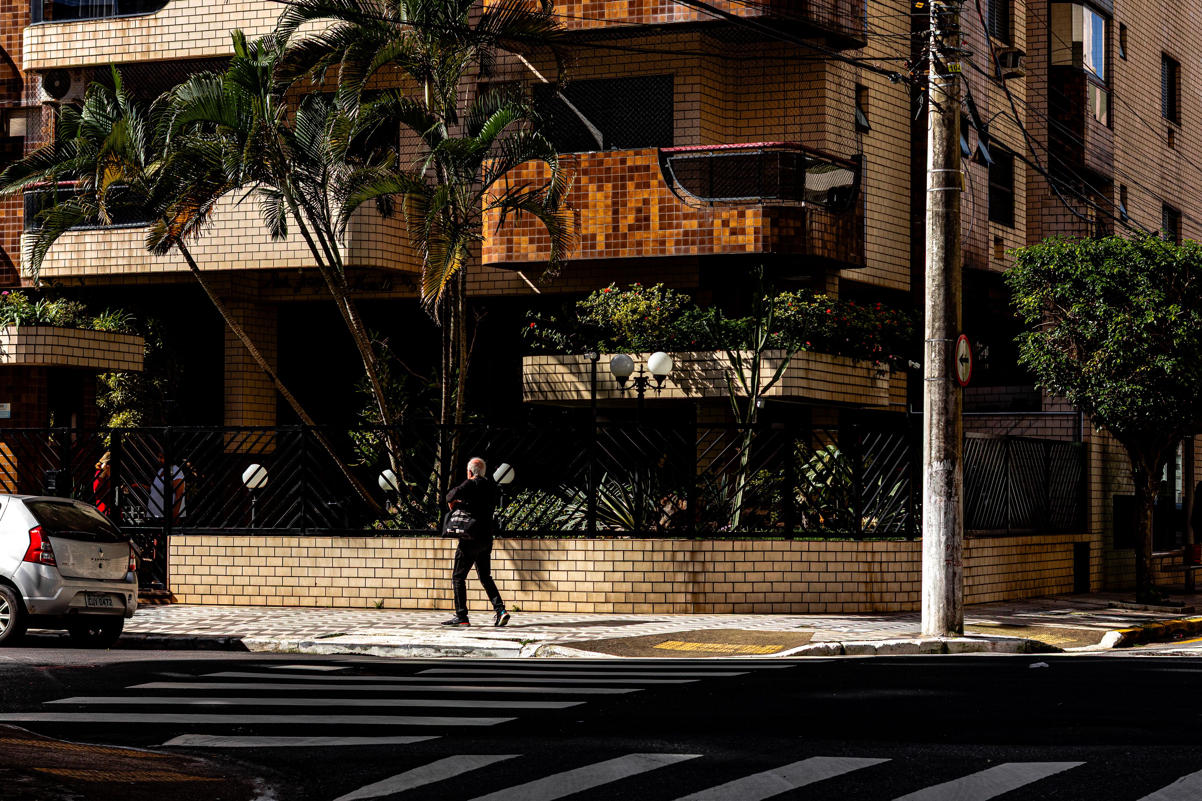 Person walking past modern urban building with palms, showcasing city life.