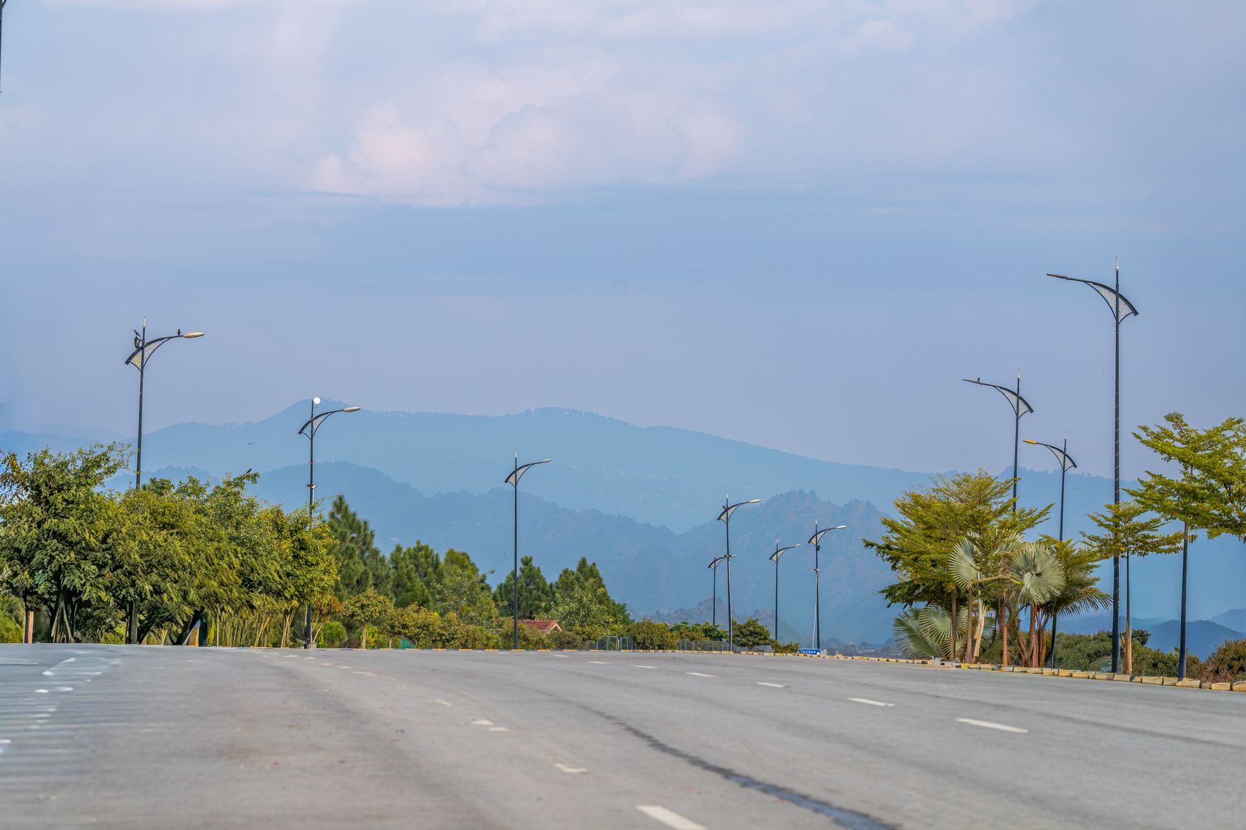 A calm boulevard lined with streetlights and trees, leading to distant mountains in Islamabad.